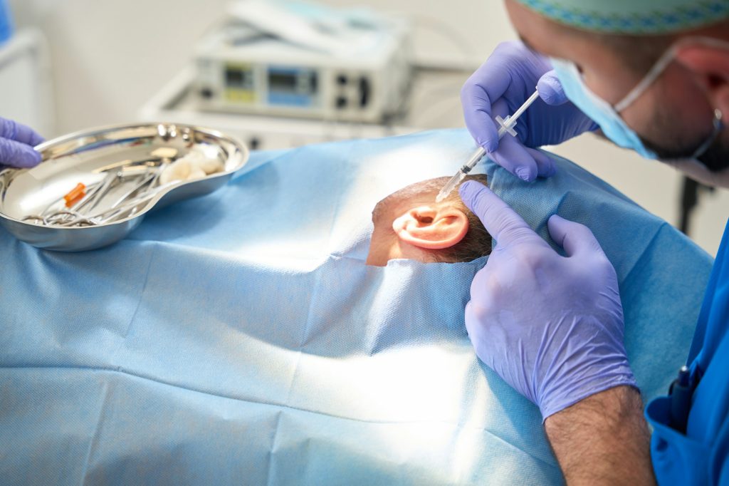 Male doctor injects syringe into ear of elderly man